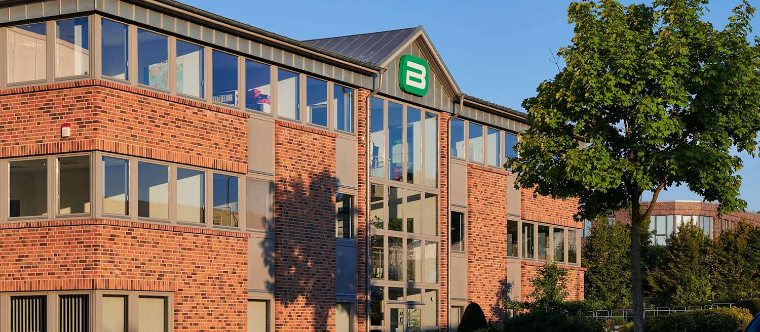 Backsteingebäude mit grün-weißem Logo und großflächigen Fenstern im Abendlicht.