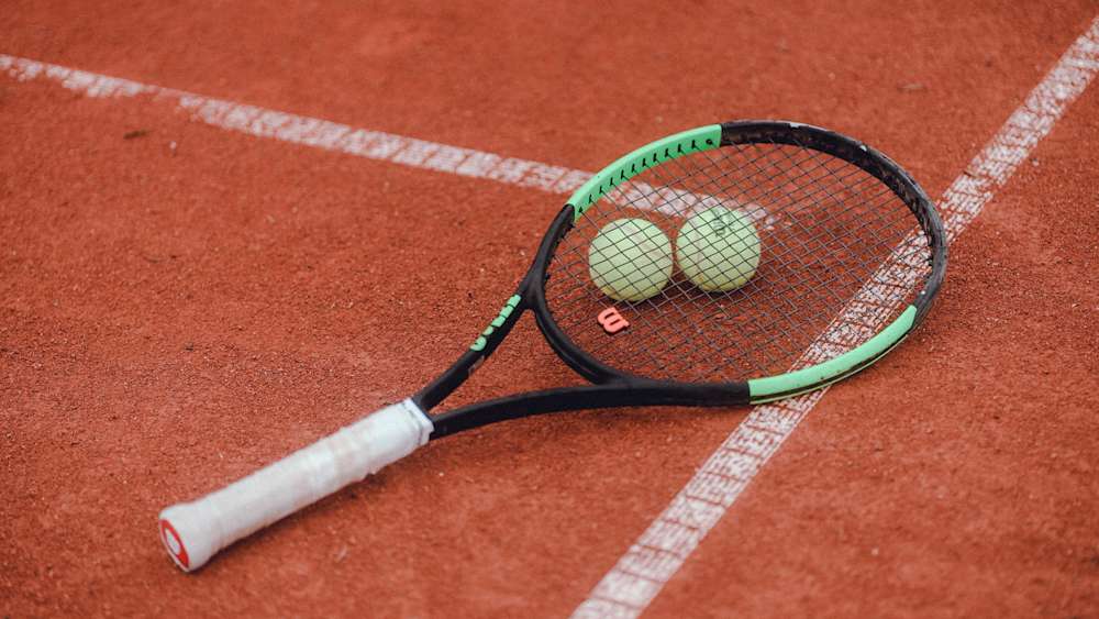 Tennisschläger und zwei Bälle liegen auf einem Hartplatz