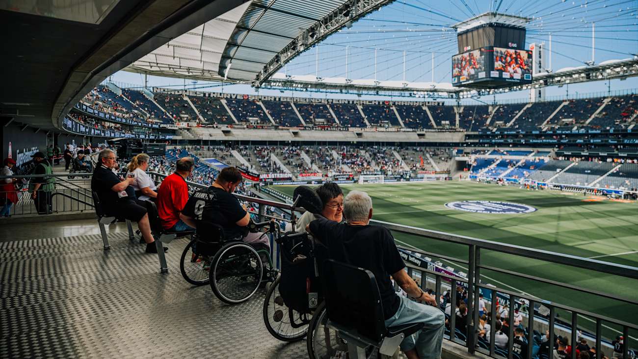 Barrierefreier Zuschauerbereich im Deutsche Bank Park mit Fans im Rollstuhl und Blick aufs Spielfeld