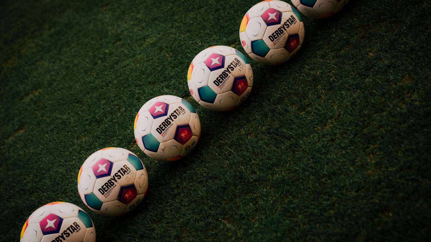 Offizielle Bundesliga-Spielbälle von Derbystar liegen in einer Reihe auf dem Rasen