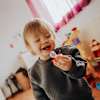 Lachendes Kleinkind hält einen roten Eintracht Frankfurt Schnuller in einem hellen Kinderzimmer.
