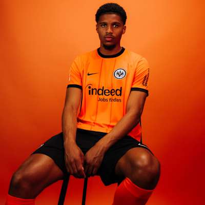 Spieler im Eintracht Frankfurt Ausweichtrikot 2024/25 in Orange mit schwarzen Akzenten vor orangem Hintergrund. Trikot Ausweich 24