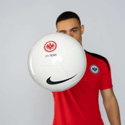 Spieler im roten Shirt mit Eintracht-Logo hält weißen Nike-Fußball mit Eintracht-Logo und Swoosh in die Kamera. Nike Fußball 24 Gr.5