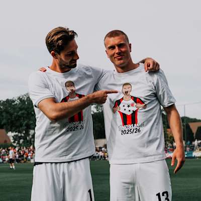 Trapp und Kristensen tragen weiße Shirts auf einem Fußballplatz mit Champions League-Motiv. T-Shirt Entfesselt