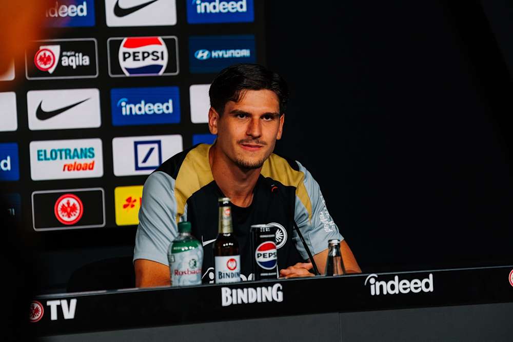 Ein Foto von Igor Matanović von einer Pressekonferenz. Er sitzt an einem Tisch und schaut nach vorne, hinter ihm die Sponsorenwand des Pressekonferenzraumes.