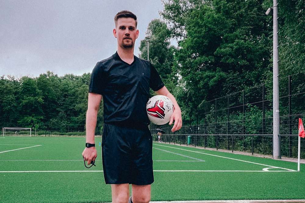 Scout Sebastian Beier steht mit einem Ball in der Hand auf einem Fußballfeld.