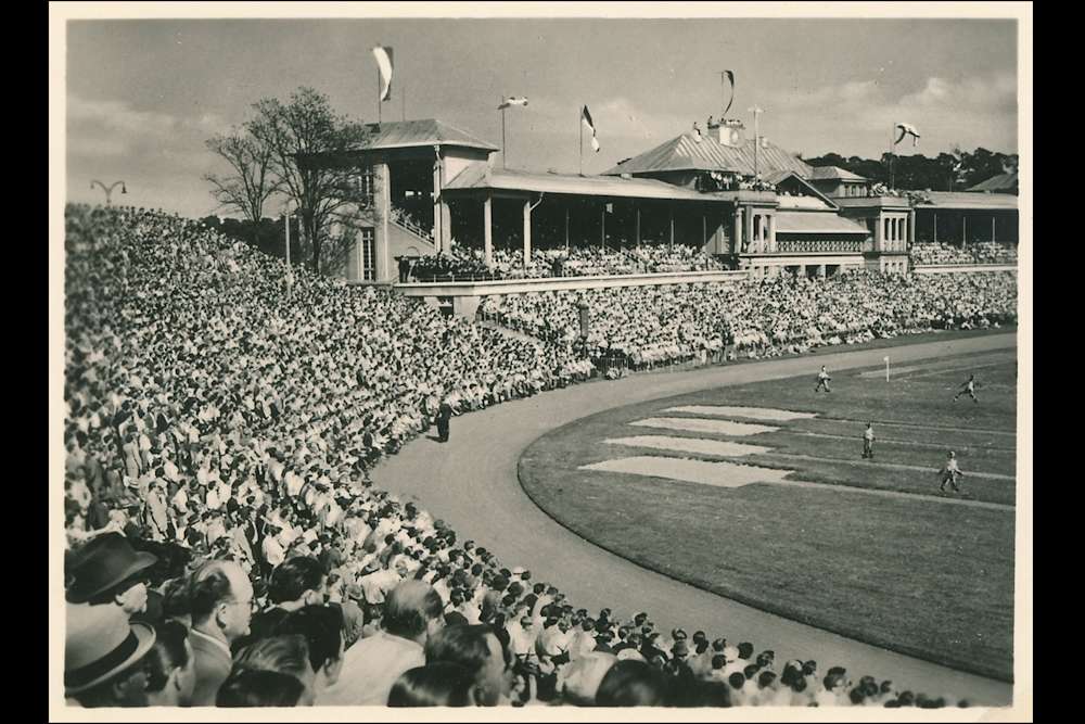 Ein schwarz-weiß Foto, aufgenommen von der Westkurve des Stadions mit Blick auf die Haupttribüne. Das Stadion ist voll besetzt mit Zuschauern, am rechten Bildrand sieht man das Spielfeld.